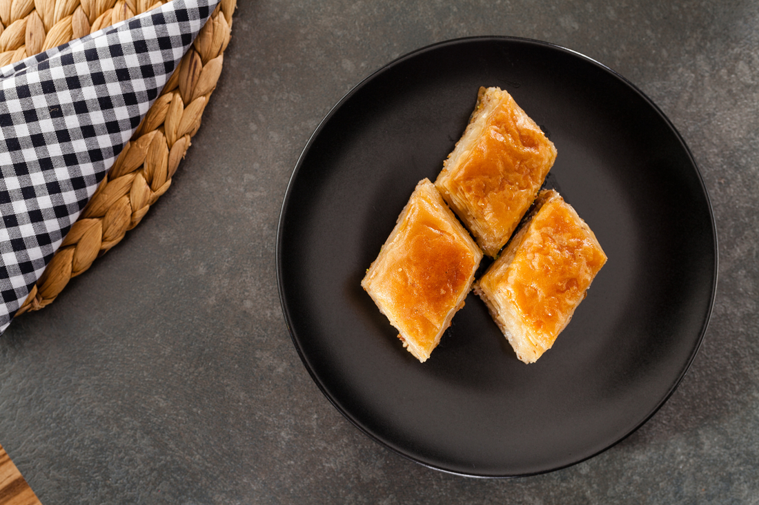 Three square pastries on a black plate with a woven basket and checkered cloth in the background.