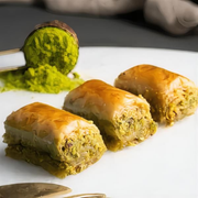 Three baklava rolls with green pistachio filling on a white plate.